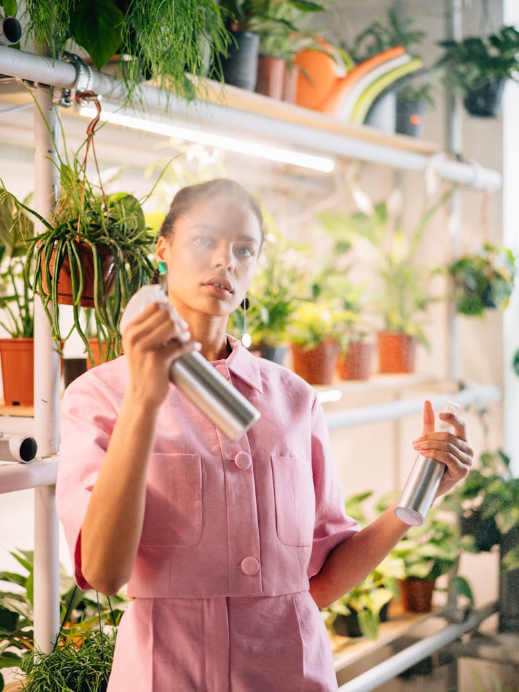 A Woman Holding A Sprayer Bottles While Standing Near The Plant Shelves