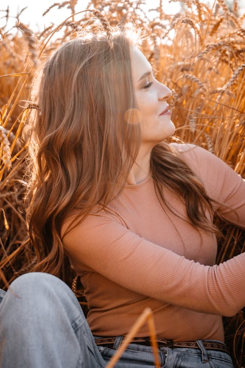 A Woman in Brown Long Sleeve Shirt and Blue Denim Jeans Sitting on Brown Grass Field 