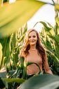 A Woman in Brown Sweater Smiling while Standing Near the Green Plants