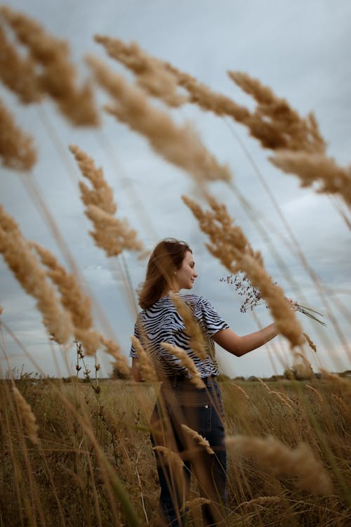 A Woman in Black and White Stripe Shirt Standing on Brown Grass Field