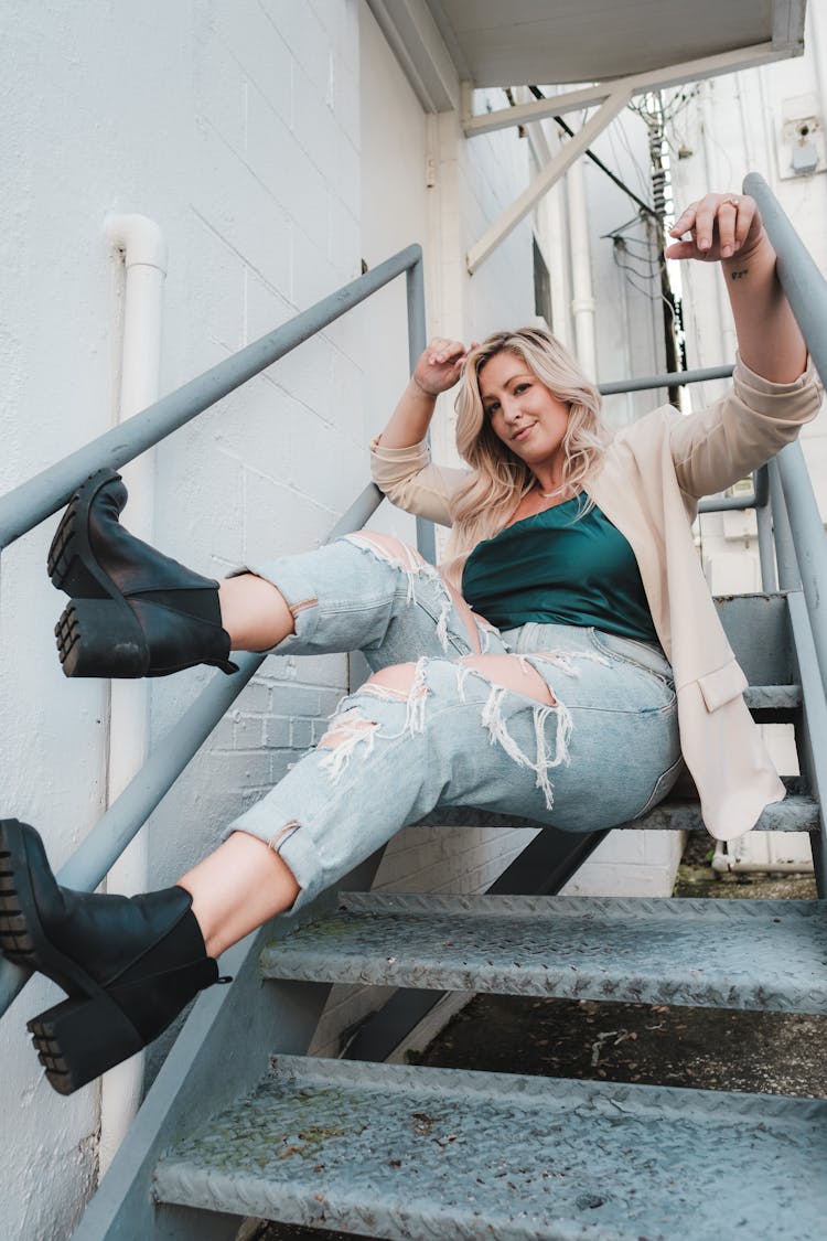 A Low Angle Shot Of A Woman In Denim Jeans Sitting On The Stairs