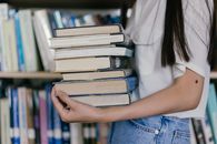 A Person in White Shirt Carrying a Stack of Books