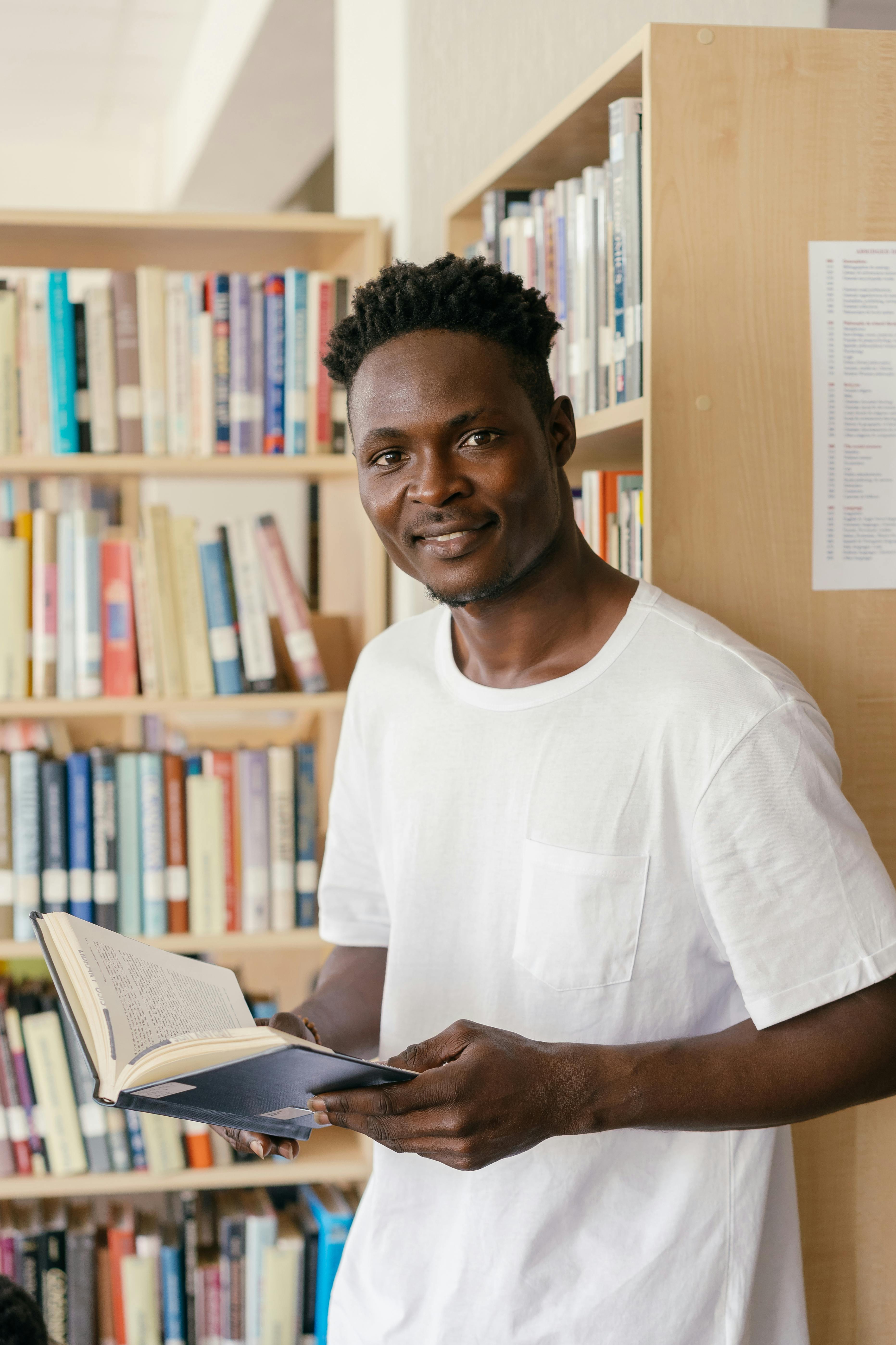 a man in white shirt leaning on the shelf while holding a book