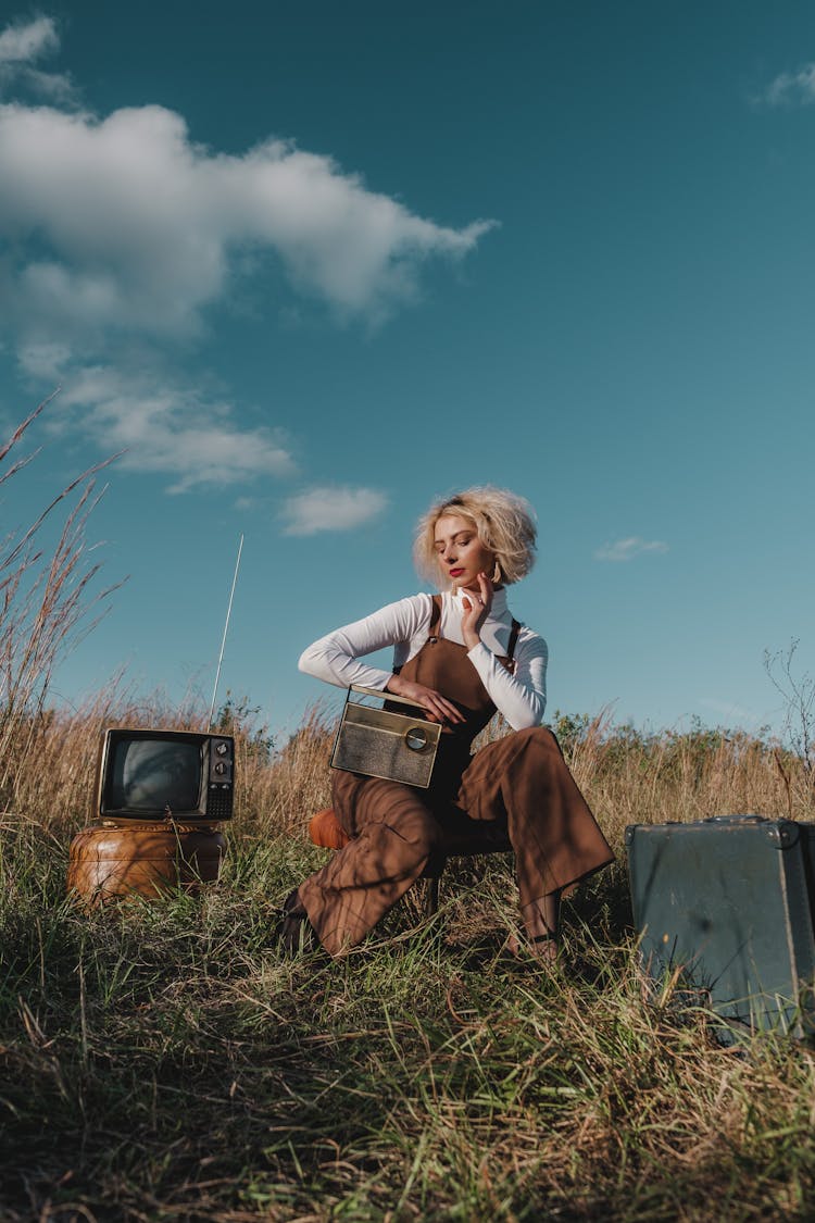 Woman In White Long Sleeve Shirt And Brown Overalls Outfit Sitting On A Stool On Grass Field