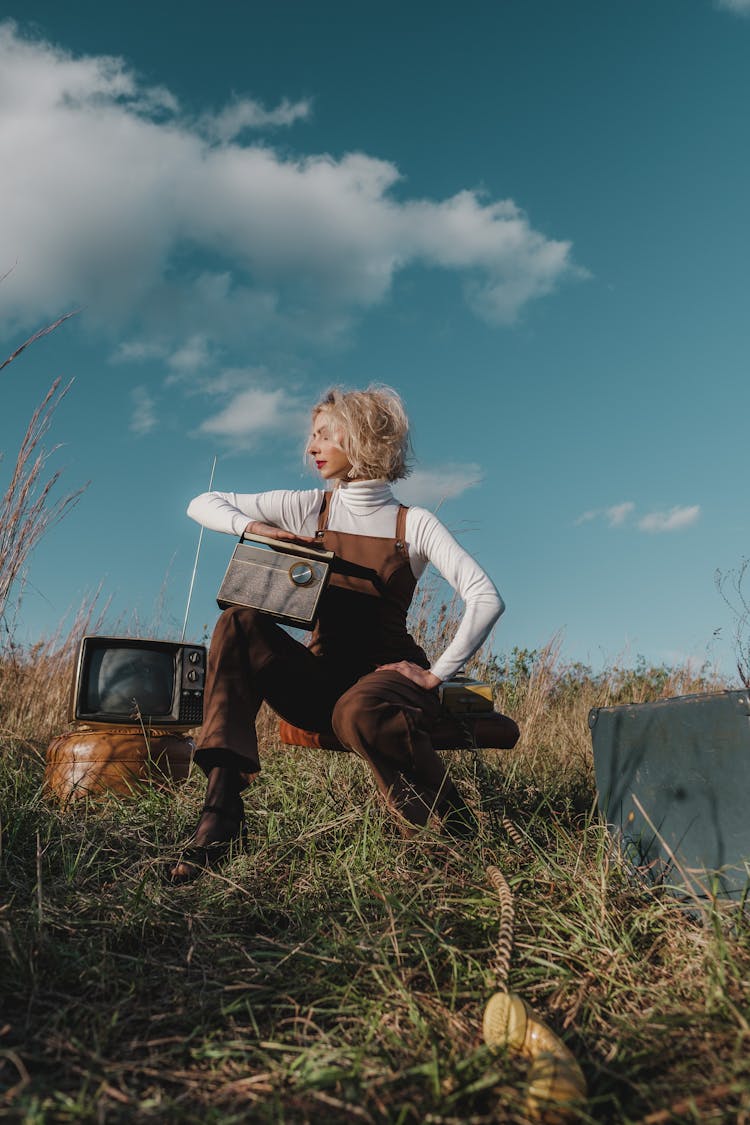 Woman In White Long Sleeve Shirt And Brown Overalls Outfit Sitting On A Stool On Grass Field