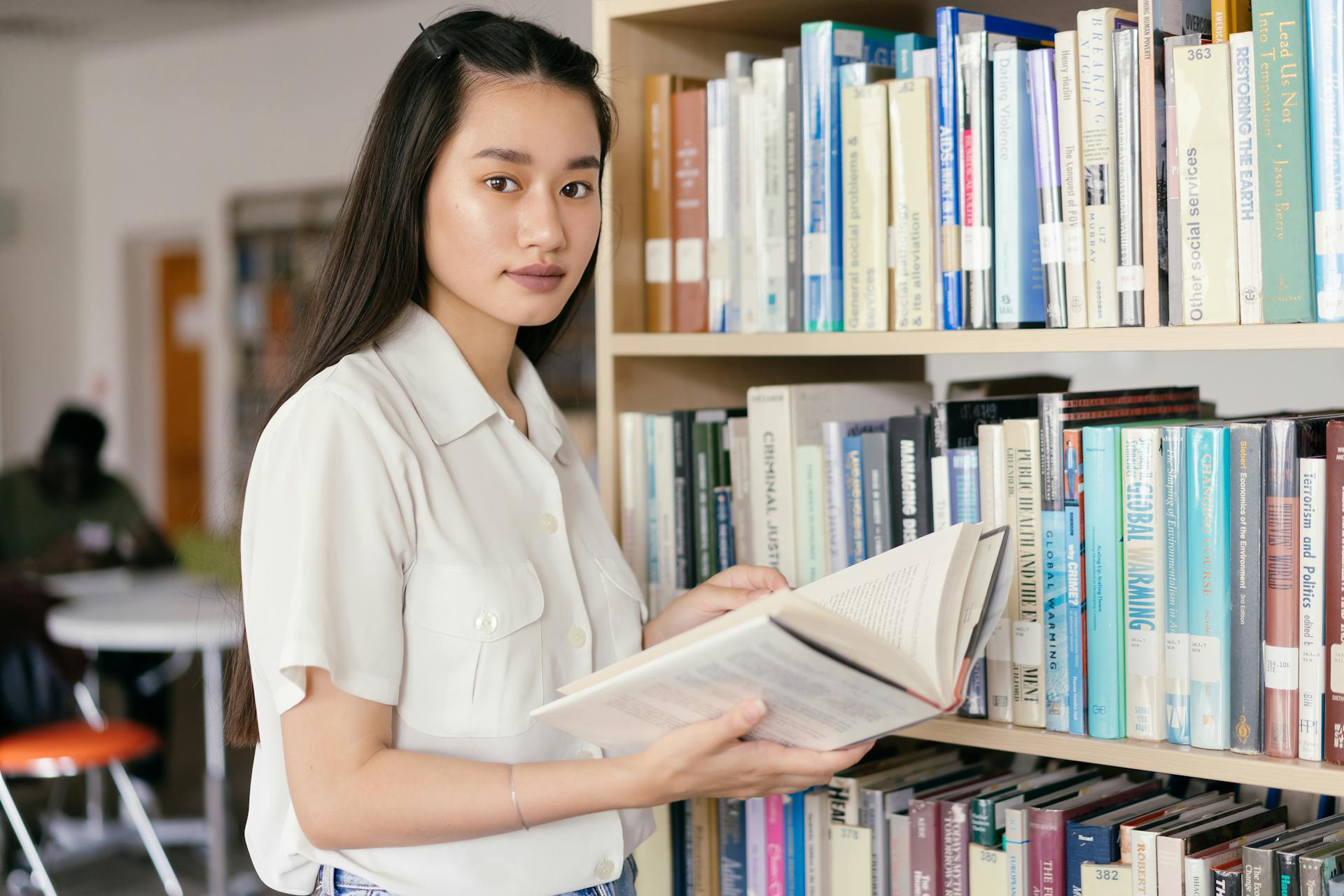 An Asian teenager reading a book in a college library, emphasizing education and learning.