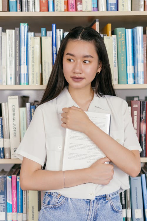 Woman Holding a Book Near a Bookshelf