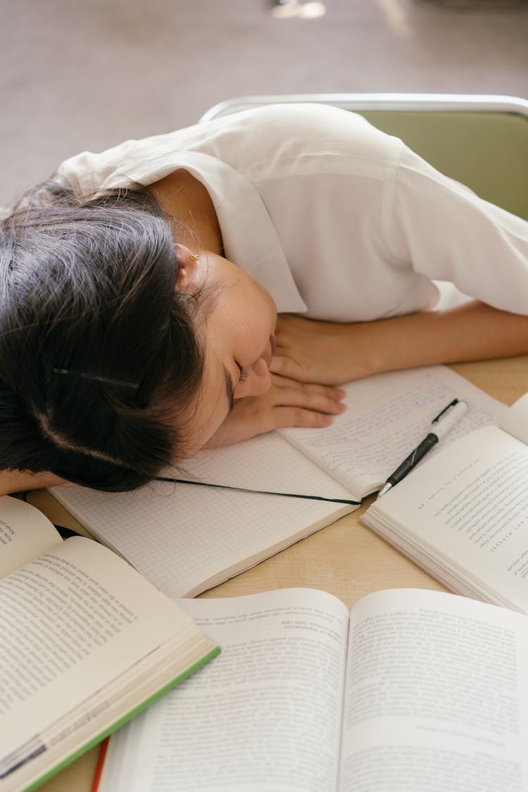 Tired Student Sleeping On Books On Desk