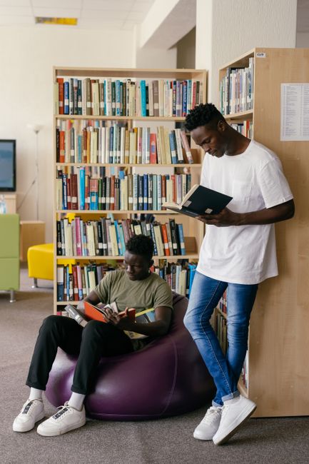Two young men engaged in reading inside a library filled with books. Two young men engaged in reading inside a library filled with books.