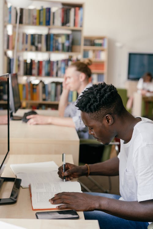 A Man in White Shirt Writing on the Book