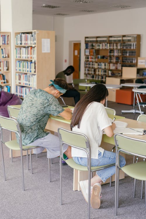 A Man and Woman Writing on the Table Inside the Library