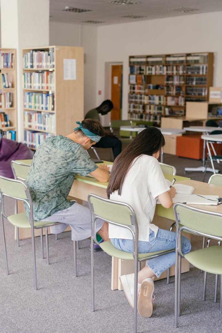 A Man And Woman Writing On The Table Inside The Library