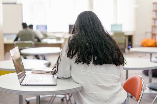 A student focused on studying at a library table with a laptop and books. Modern and educational atmosphere.