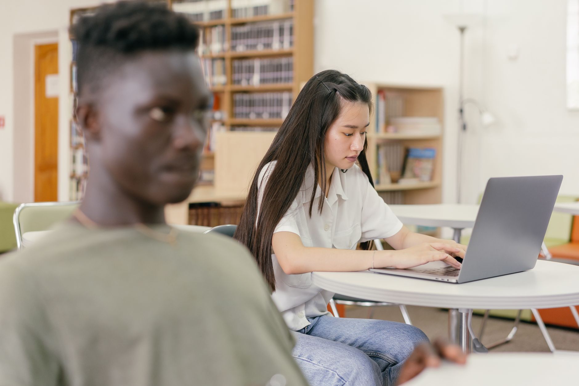 Two students focused on study in a contemporary library setting with laptops and books.