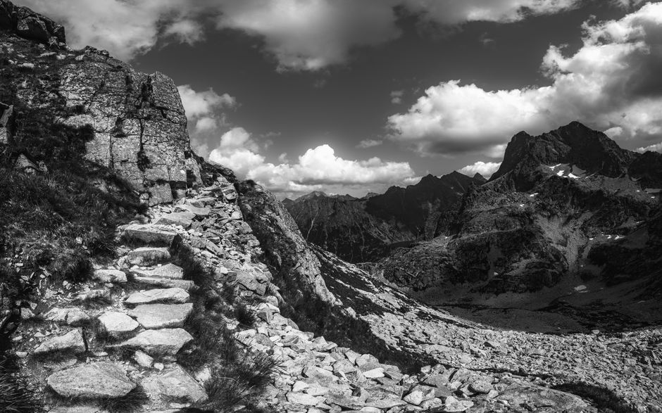 Stunning black and white landscape showcasing a rocky mountain pathway under dramatic clouds.