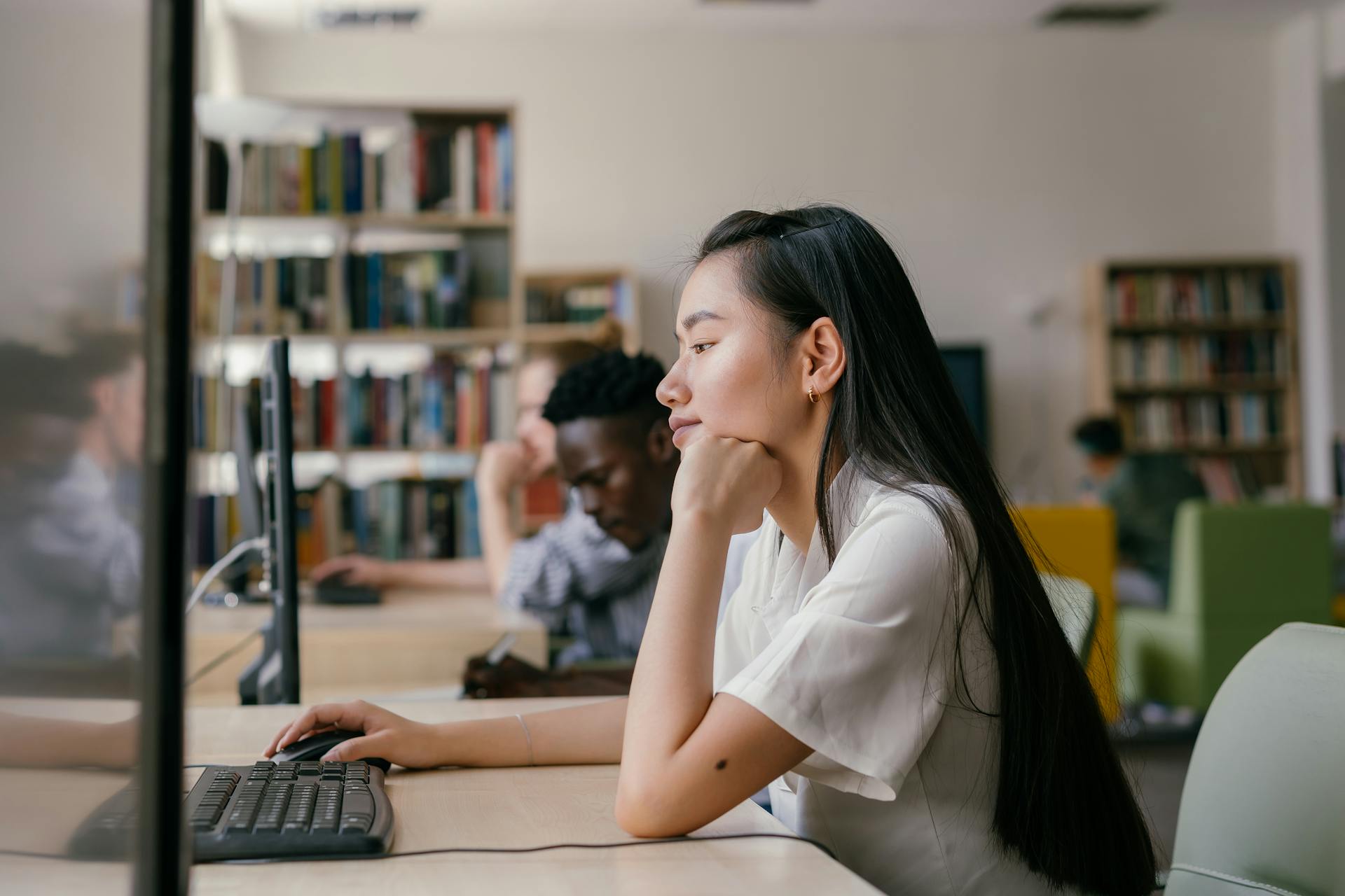 Asian woman studying diligently on a computer in a vibrant university library setting.