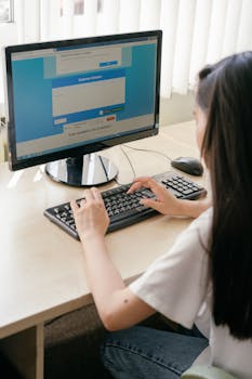 A student typing on a computer in a bright classroom for e-learning or research.