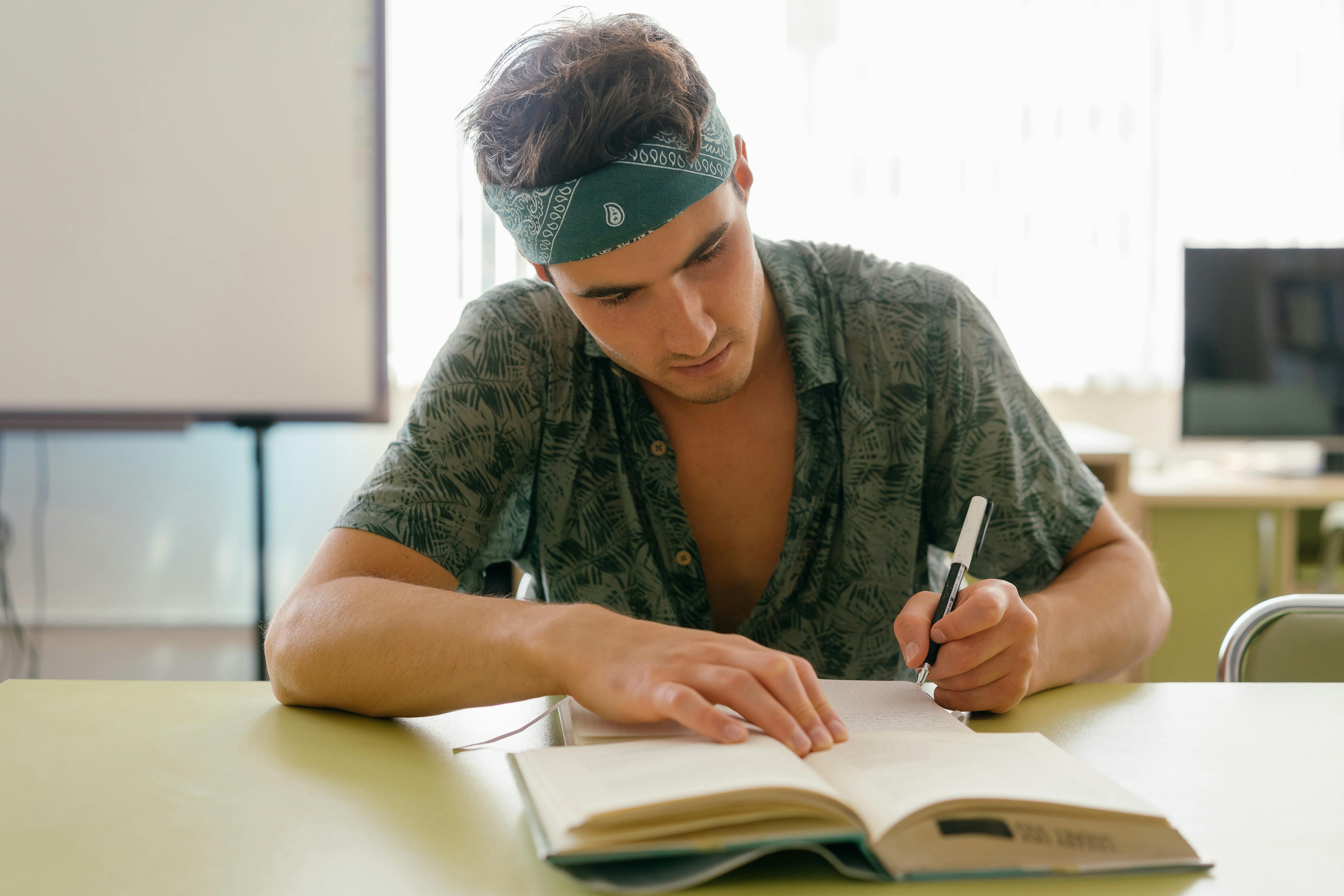 a man with bandana writing on the white notebook