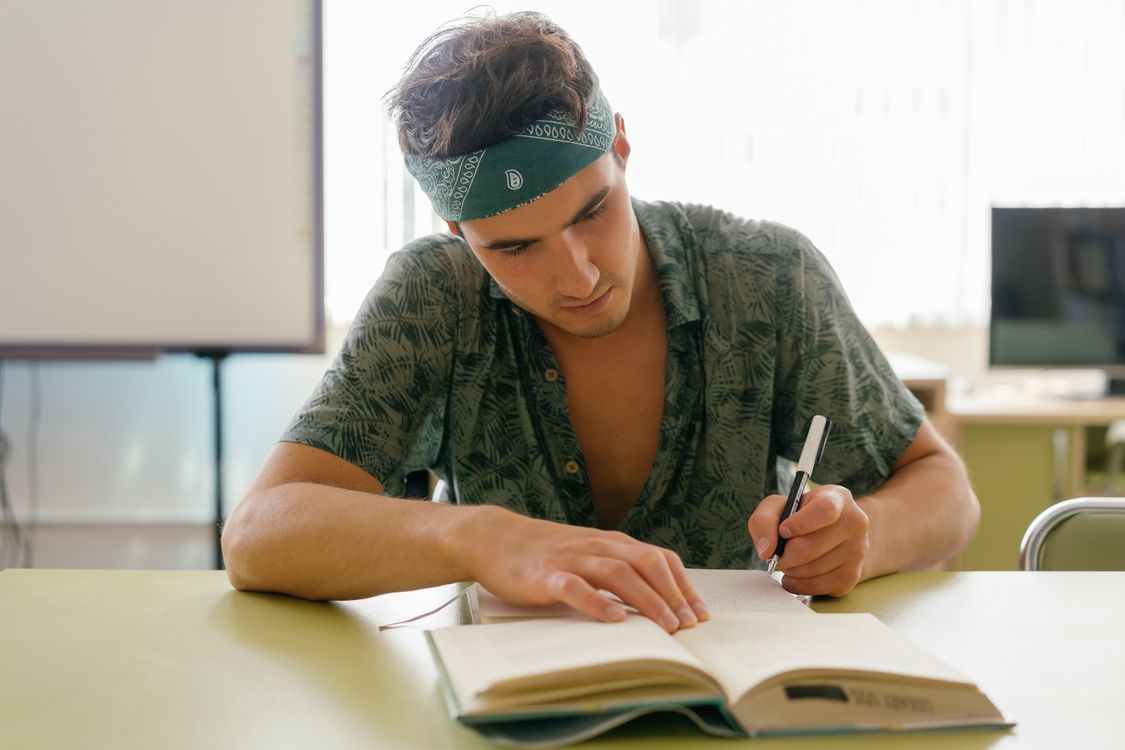 A Man with Bandana Writing on the White Notebook