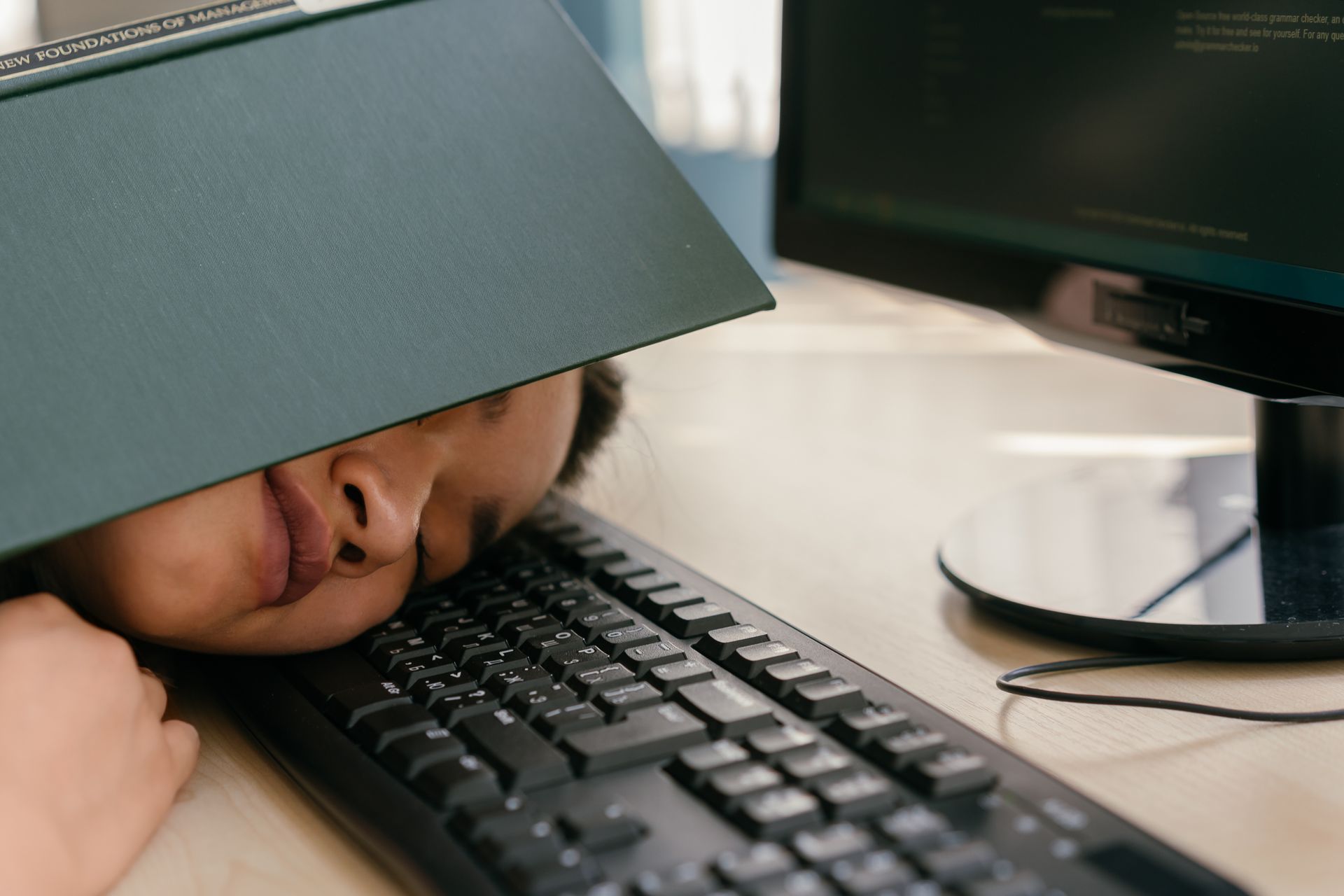 Young Woman Sleeping on Computer Keyboard with a Book on Her Head