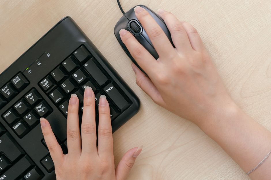 Primer plano de manos en un teclado y ratón, destacando la configuración de trabajo en la oficina.