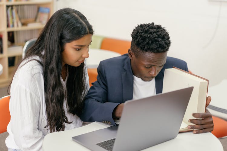 A Teacher And A Student Sitting At Desk Reading A Book