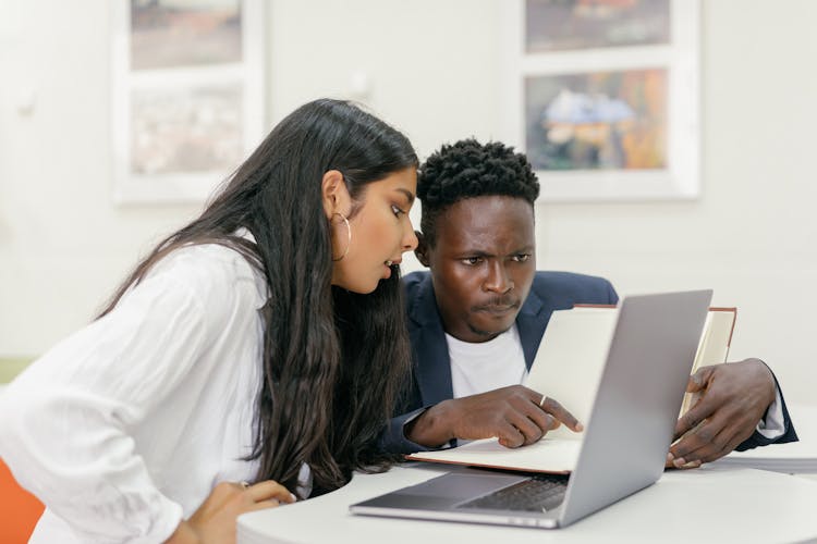 A Professor And A Student Sitting At A Desk With A Computer  And A Book 