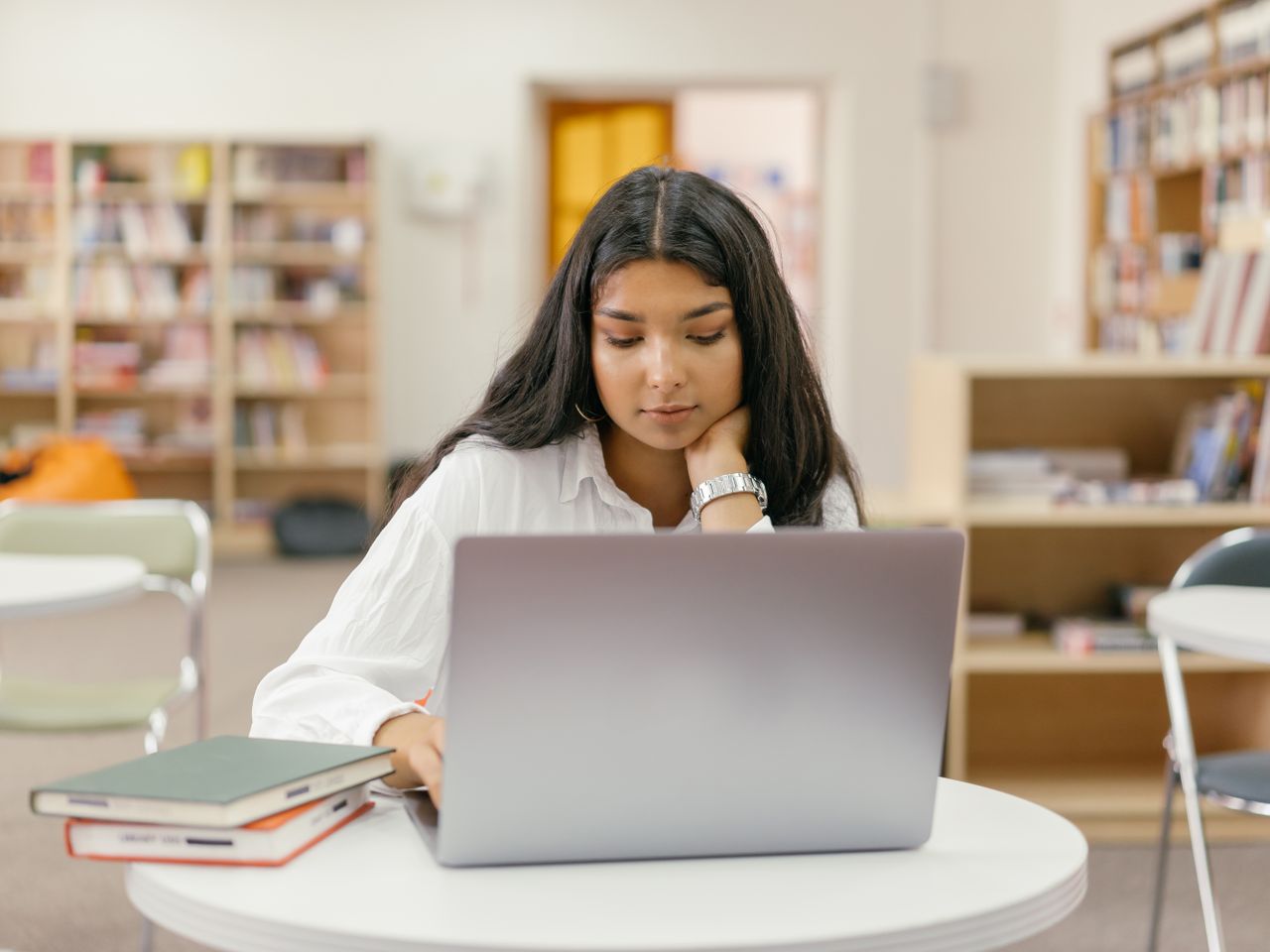 A Black female student studying at a library desk with books open