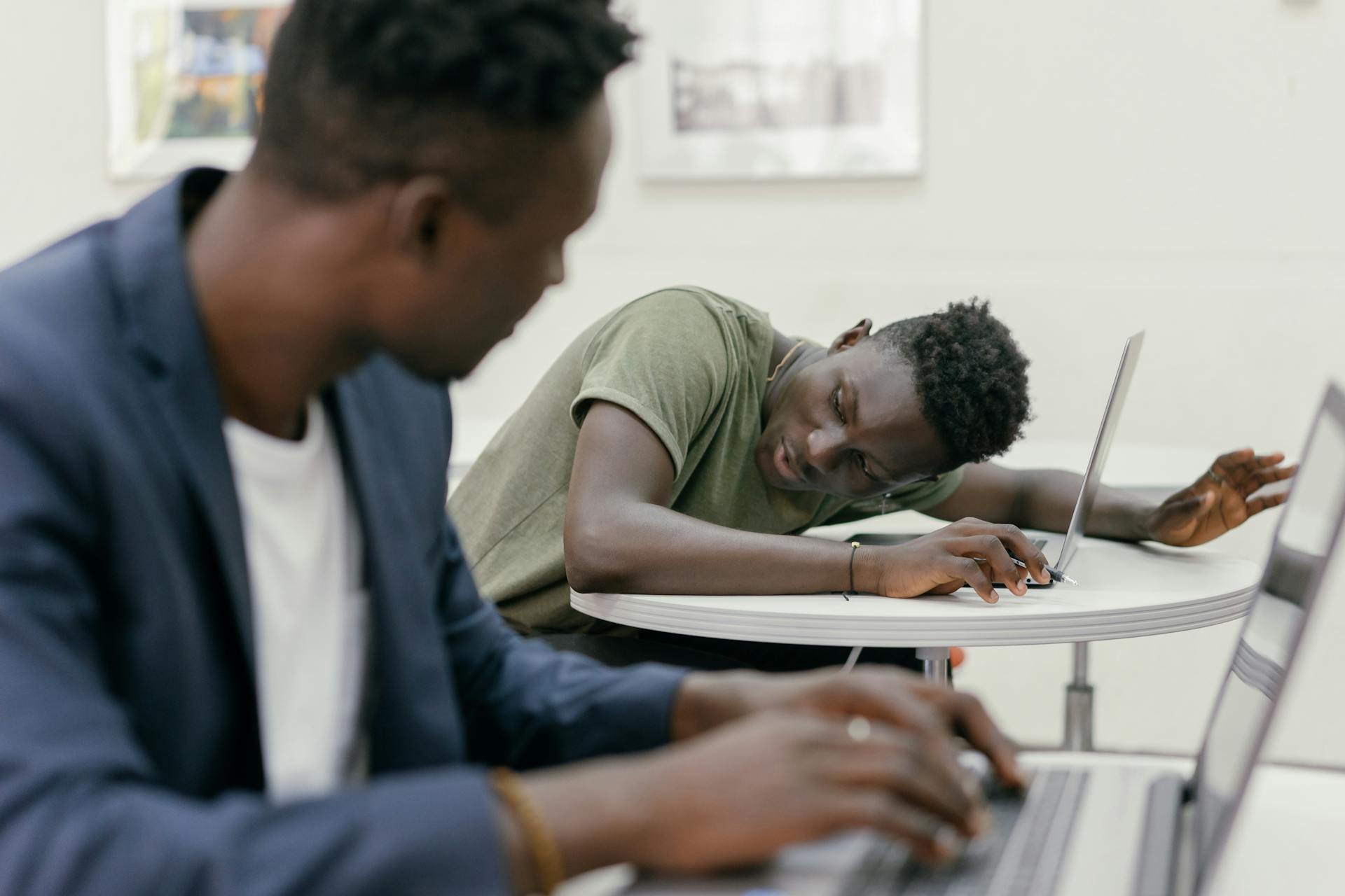 Two young men using laptops at a table, focused on online studies.