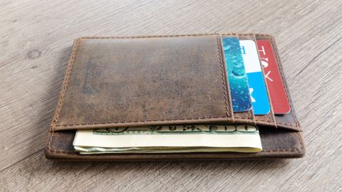 A brown leather wallet with cash and credit cards on a wooden surface.