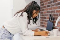 A Woman in White Long Sleeves Reading a Book at the Kitchen