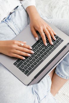 A woman with manicured nails types on a laptop, showcasing modern technology.