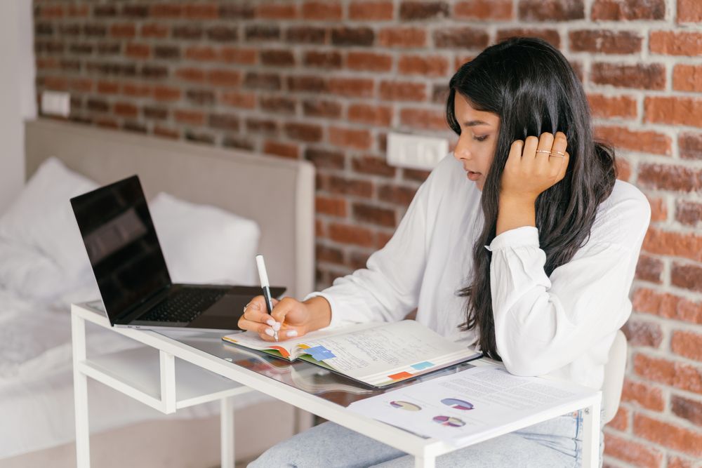 Student working at a home desk with a laptop and an open notebook. Photo by Mikhail Nilov on Pexels