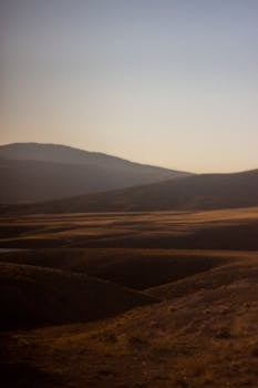 A tranquil scene of rolling hills at dawn with a soft light casting gentle shadows.