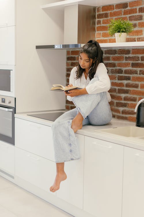 A Woman Holding a Book While Sitting on the Kitchen Counter Top