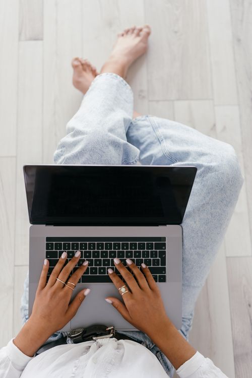 Free Overhead view of a woman typing on a laptop while sitting cross-legged indoors. Stock Photo