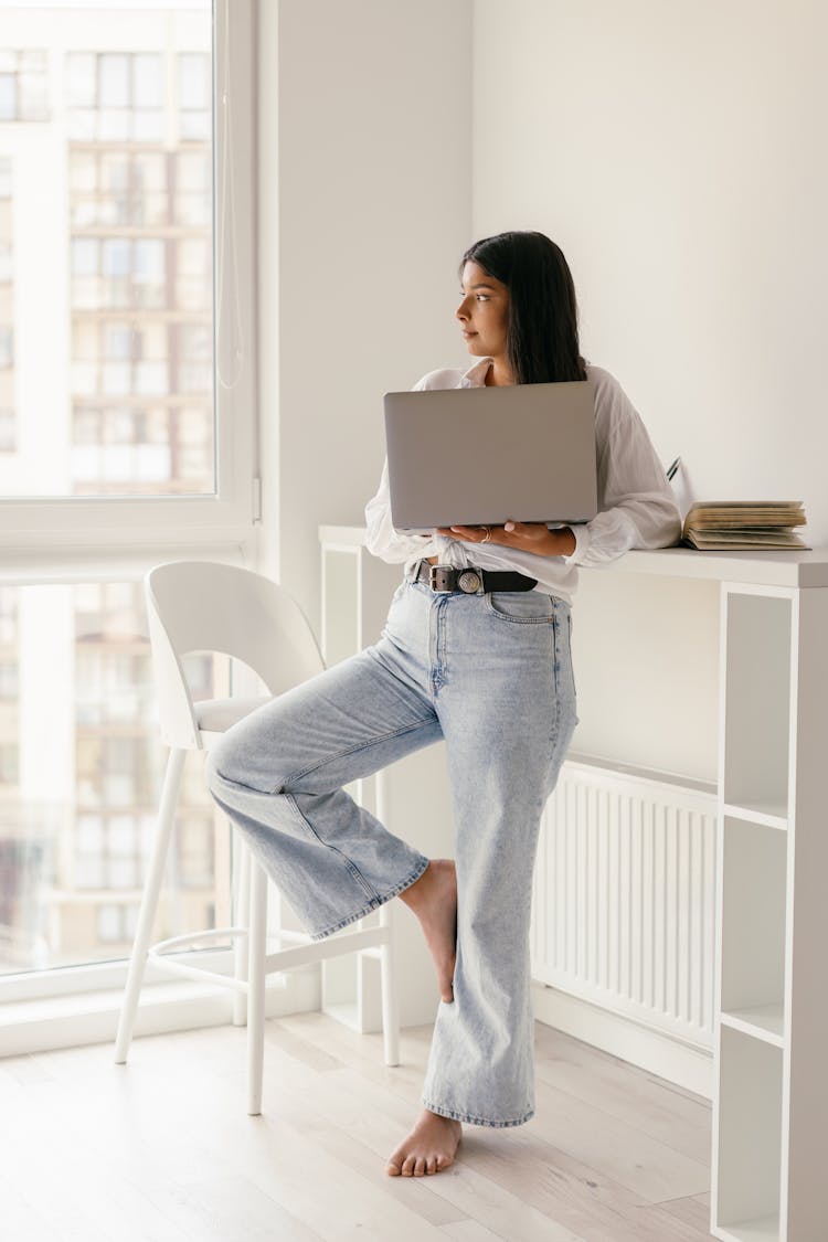 Young Brunette Woman Standing In Home With Laptop In Hand