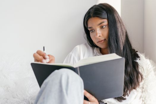 Contemplative young woman writing in a journal indoors, capturing a moment of reflection and learning.