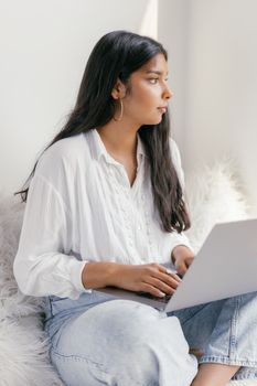 Young woman focusing on work while sitting with a laptop on a cozy couch indoors.