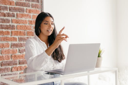 Woman working from home on a laptop, pointing at screen during a video call.