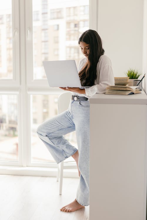 A Woman Using a Laptop While Standing Near a Cabinet