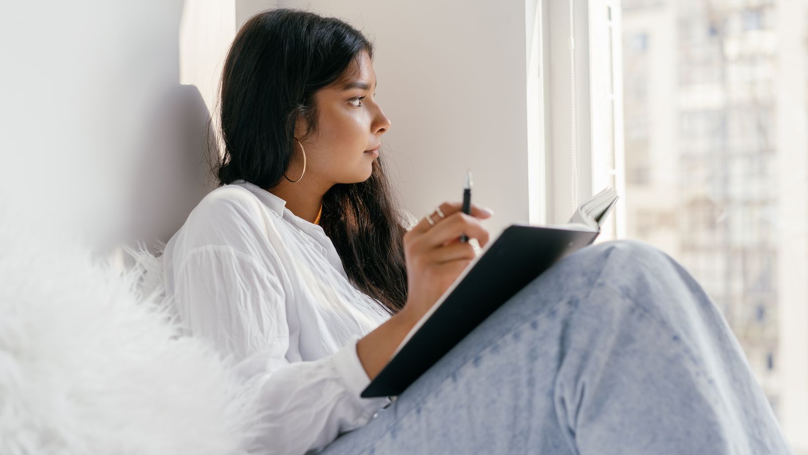 An adult reflecting with a notebook beside a window