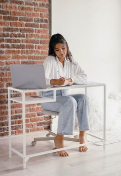 Woman studying at a modern desk with laptop, focused on writing.