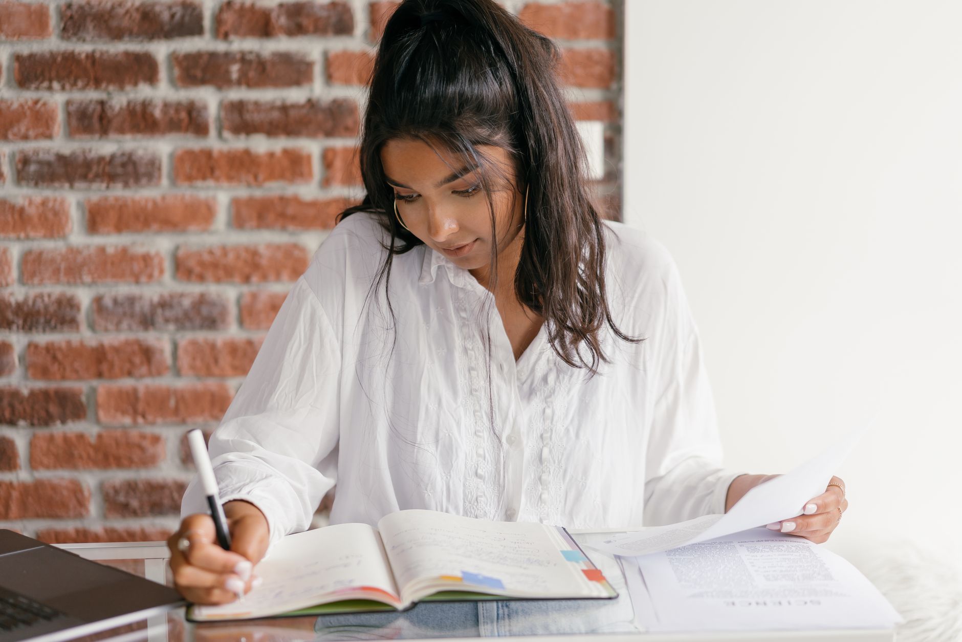 Young woman studying with books and a laptop in a cozy indoor setting, focusing on her work.