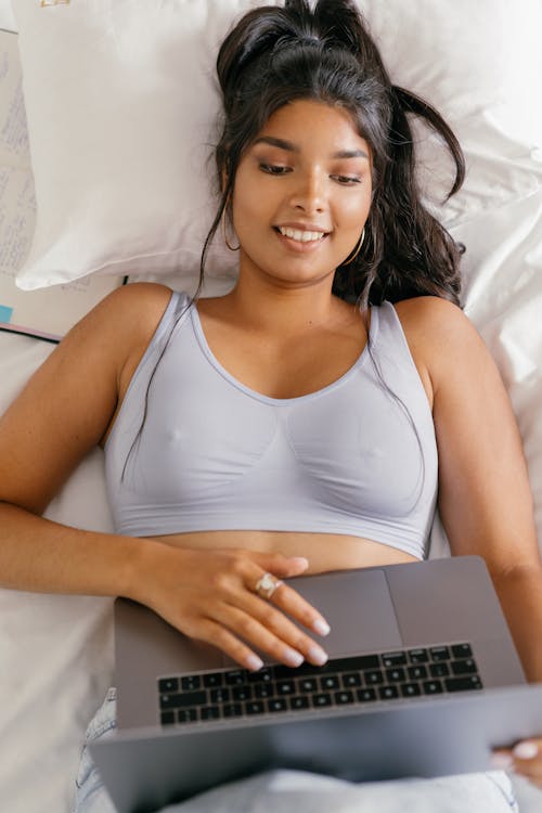 Woman in Tank Top Lying on Bed While using a Laptop
