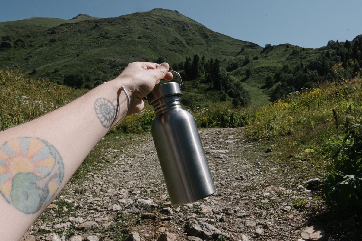 hiker holding a stainless steel reusable water bottle on a mountain trail