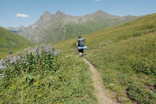 Free A lone hiker walks through a scenic mountain trail surrounded by lush greenery. Stock Photo