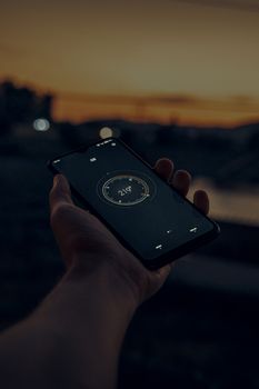A person holding a smartphone displaying a compass app at sunset.