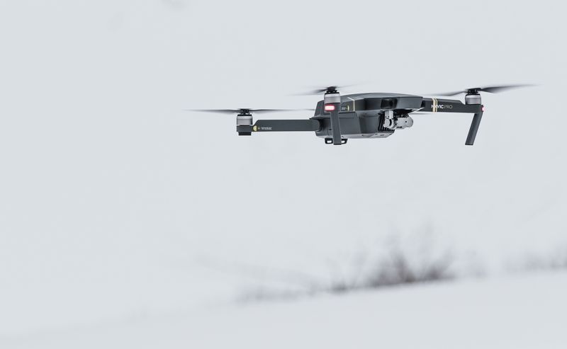 A quadcopter drone in flight over snow-covered ground