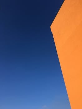 Striking minimalist composition featuring an orange building against a vivid blue sky.